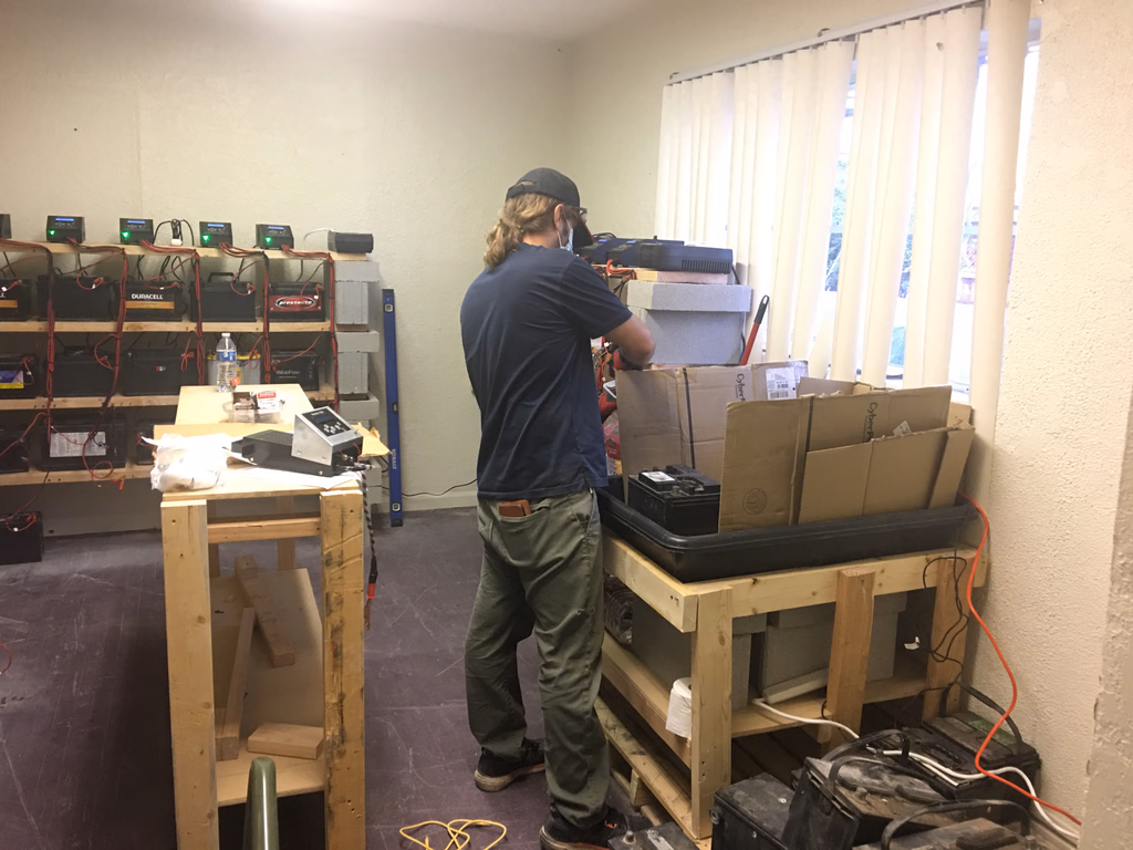 A ReVolt Battery Exchange technician reconditioning batteries at a workbench